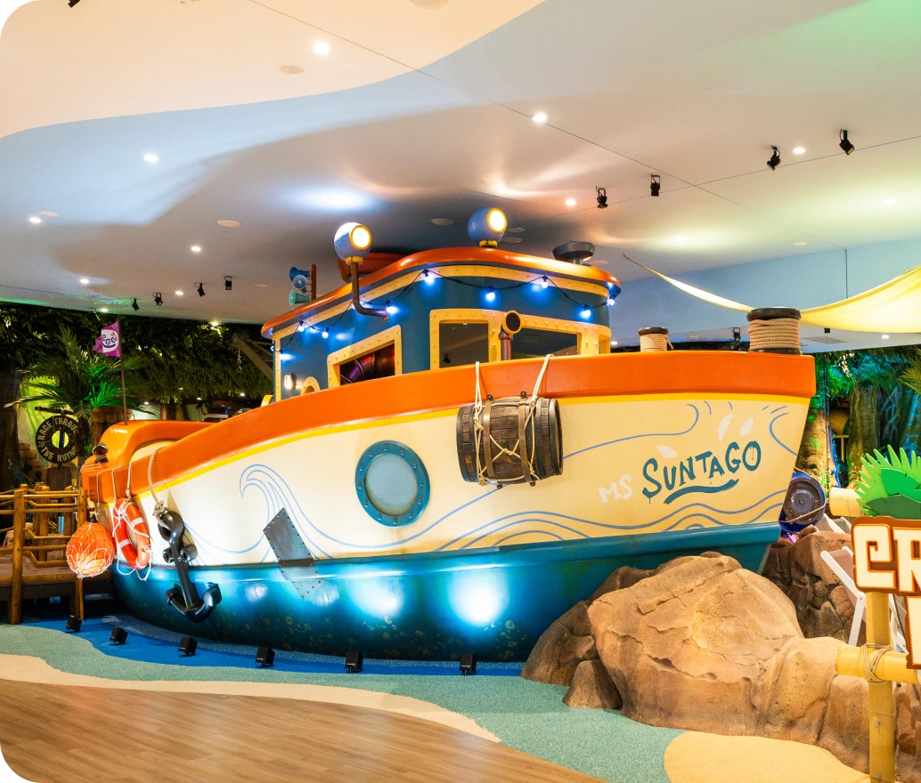 Colorful play boat 'MS SUNTAGO' anchored indoors, children's play centerpiece with decorative details.