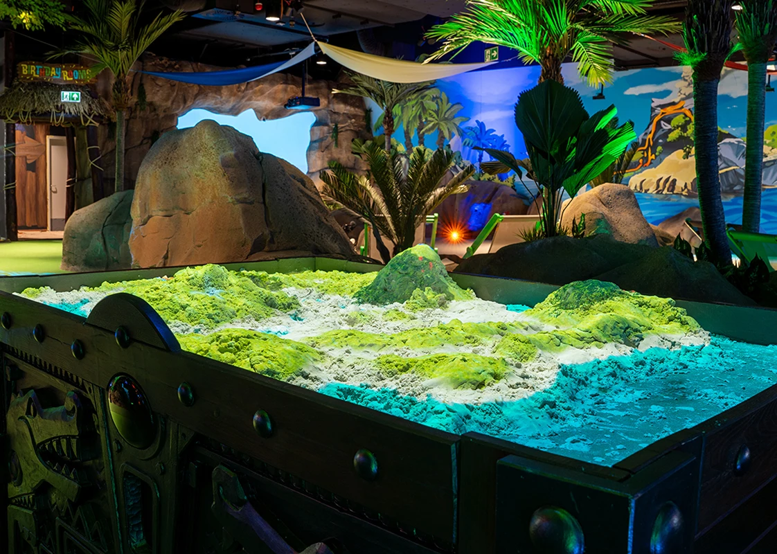 Raised sand play table sculpted into mounds, bathed in vivid blue and green lighting.