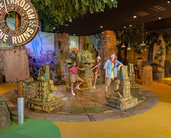 Kids exploring an indoor ruins-themed play area with carved stone pillars and warm lighting.