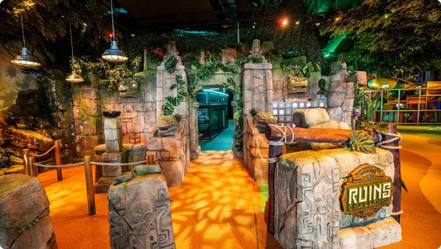 Stone archway leading into a jungle-themed play maze, overhead lamps casting warm light, mysterious feeling.