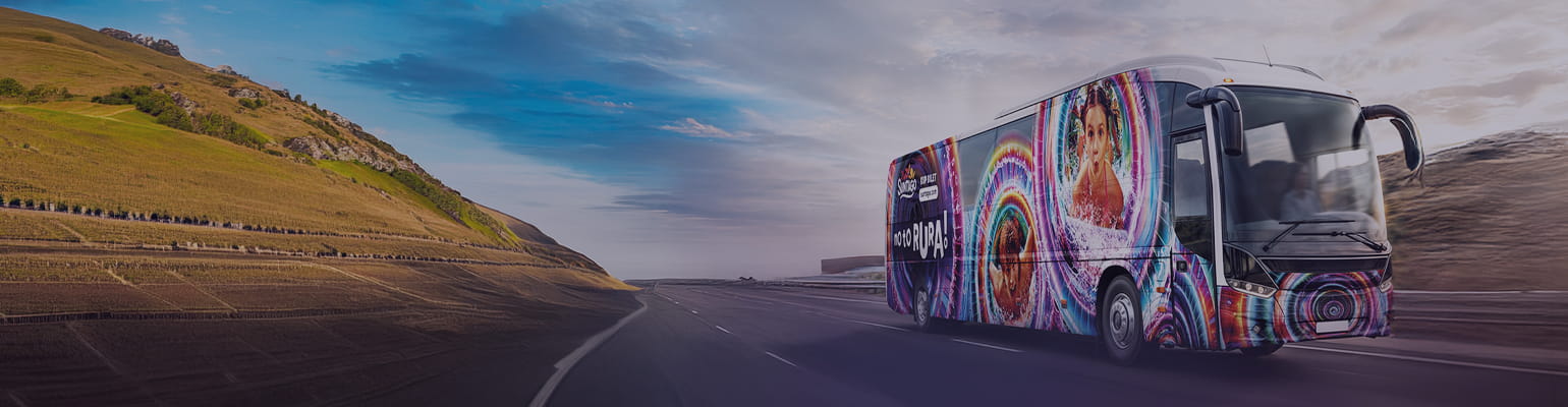 Suntago bus decorated with palm tree graphics. The side of the bus displays the text "Buy a ticket at parkofpoland.com". In the background, silhouettes of palm trees against the setting sun.