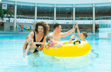 A family of five enjoying a sunny day in a water park pool, playing with a yellow raft