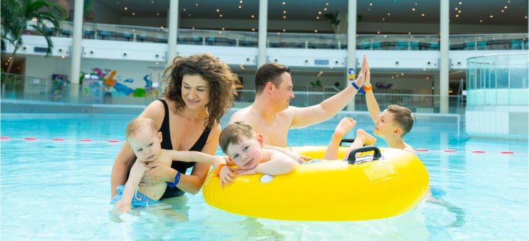 A family of five enjoying a sunny day in a water park pool, playing with a yellow raft