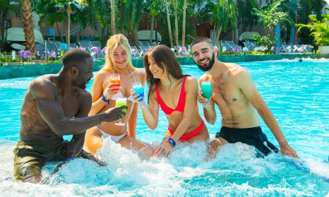 Group of friends at Suntago, sitting in the pool, enjoying colorful drinks, surrounded by tropical plants