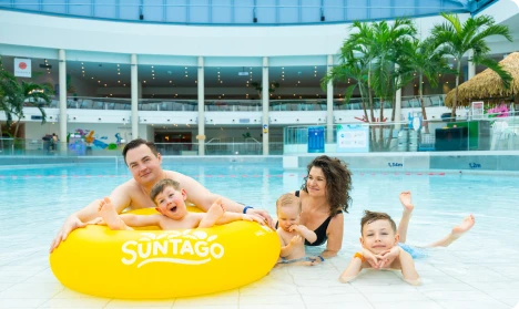 Family in the Jamango zone pool, parents and kids on a yellow float in a water park with tropical plants