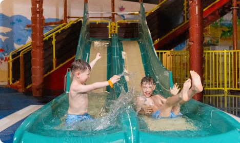 Two boys on a water slide at an indoor water park, smiling and enjoying their time