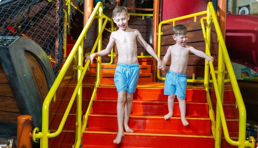 Two smiling boys walking down colorful slide stairs at Suntago