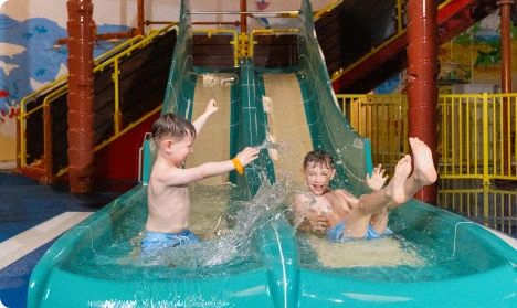 Two boys on a water slide at an indoor water park, smiling and enjoying their time