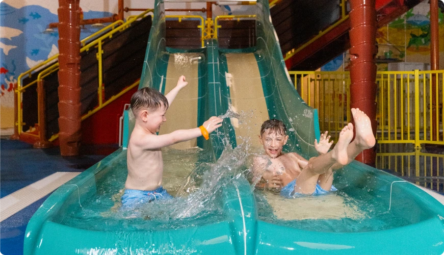 Two boys on a water slide at an indoor water park, smiling and enjoying their time