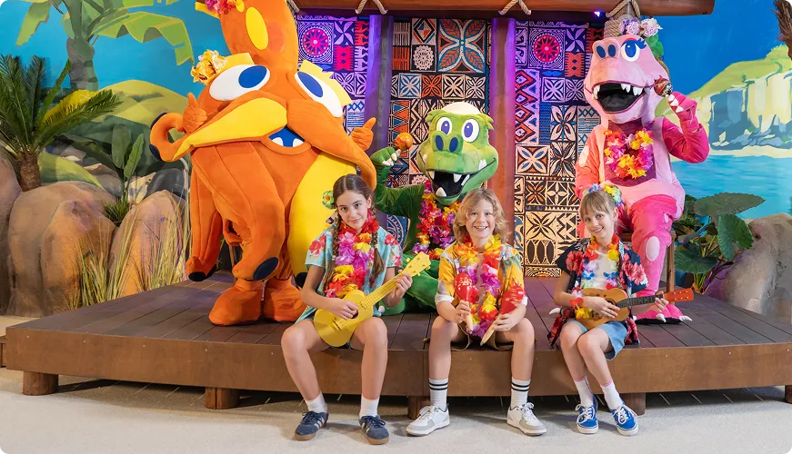 Children with dinosaur, crocodile and hippopotamus mascots in tropical setting with ukuleles