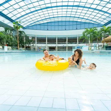 Family in the Jamango zone pool, parents and kids on a yellow float in a water park with tropical plants