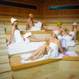 Group of friends relaxing in the Relax zone sauna, wearing traditional sauna hats and towel