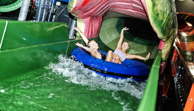 Two young people sliding down a green water slide together