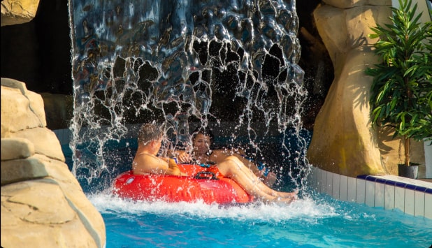 Two people sailing in a pontoon through a water curtain in a sunny setting