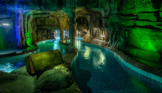 Relaxing indoor pool featuring a rock wall lit in green and blue