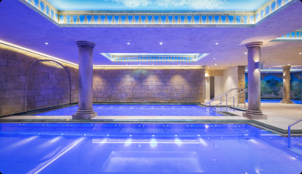 Two indoor pools with cool blue lighting and decorative ceiling