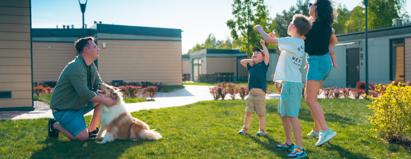 A cheerful family having fun with their dog in the green yard next to bungalow